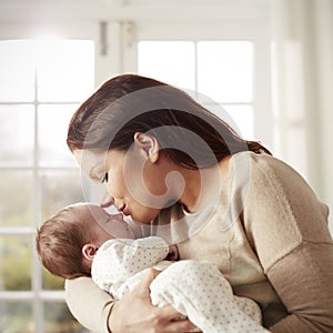 Loving Mother Kissing And Cuddling Newborn Baby At Home