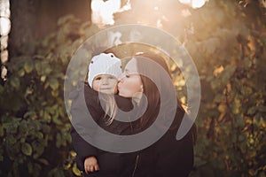 Loving mother kissing her daughter in autumnal forest.