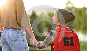Loving mother and little son schoolboy with backpak holding hands while going to school together