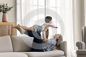 Loving mother lying on couch play with little adorable daughter