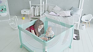 Loving mother playing with infant girl in playpen