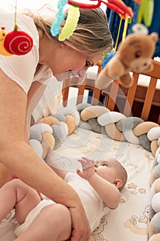 A loving mother puts her child in a crib with a musical toy. Mom hugs her baby. Happy childhood and motherhood.