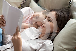 Loving mother reading book to sleepy cute little daughter