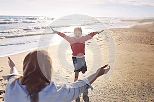 Loving mother stretched out arms to side of smiling daughter running towards her on sunny beach