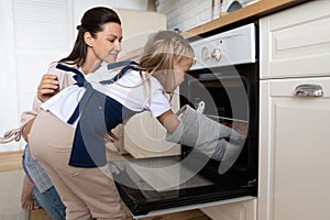 Loving mother teaching little daughter to bake cupcakes in oven