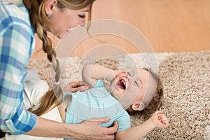 Loving mother tickling her little kid on carpet at home