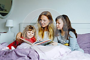 Loving mother and two little girls reading book together. Happy family, woman and cute daughters, toddler sister and