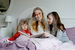 Loving mother and two little girls reading book together. Happy family, woman and cute daughters, toddler sister and