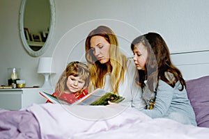 Loving mother and two little girls reading book together. Happy family, woman and cute daughters, toddler sister and