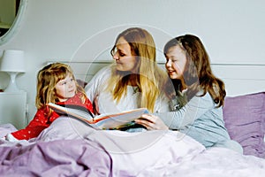 Loving mother and two little girls reading book together. Happy family, woman and cute daughters, toddler sister and