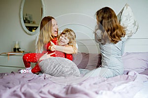 Loving mother and two little sisters girls making pillow fight together. Happy family, woman and cute daughters, toddler