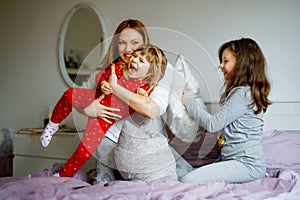 Loving mother and two little sisters girls making pillow fight together. Happy family, woman and cute daughters, toddler