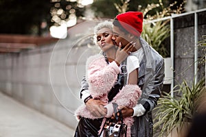 Loving mulatto couple embrace each other while have walk outdoor, kiss. Dark skinned stylish male in trendy red hat hugs