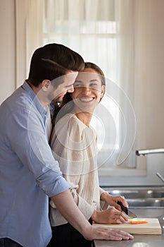 Loving newlyweds cuddle in kitchen cooking together