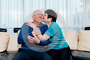 Loving older wife kissing smiling husband on cheek, expressing love and care, aged senior couple enjoying tender moment.