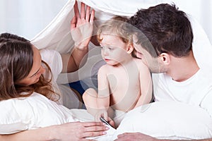 Loving parents with sad baby in bed