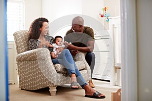 Loving Parents Sitting In Chair Cuddling Baby Son In Nursery At Home