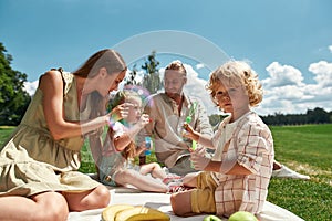 Loving parents spending time with two little kids, blowing soap bubbles in the park. Family having picnic in nature on a