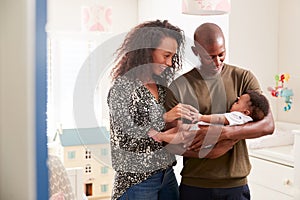 Loving Parents Standing In Nursery Cuddling Baby Son At Home