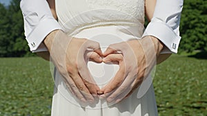 Loving parents to be making a heart shape with their hands on pregnant belly.