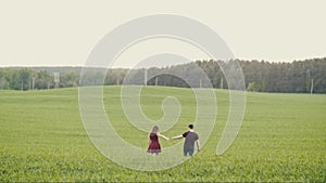 Loving people hold hands and kiss as they walk in an oat field. Happy couple in love. Forest at the background. Slow mo