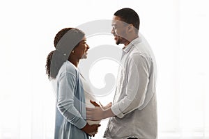 Loving pregnant black couple cuddling while spending time at home