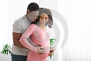 Loving pregnant couple cuddling while spending time at home