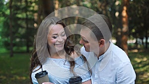 Loving Pregnant Couple with Cups of Tea in Park