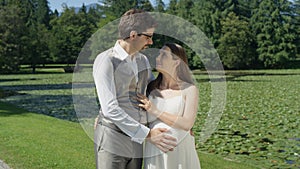 Loving pregnant couple embracing gaze into each others eyes in sunlit green park