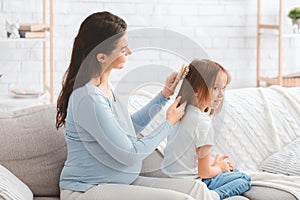 Loving pregnant woman combing her little daughter hair