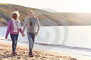 Loving Retired Couple Holding Hands As They Walk Along Shoreline On Winter Beach Vacation