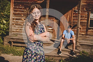 Loving romantic couple in the village, near a wooden house. A man sits on the porch, a young woman in the foreground