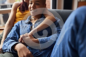 Loving Same Sex Female Couple Holding Hands Lying On Sofa At Home Watching TV And Relaxing Together