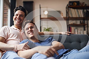 Loving Same Sex Male Couple Lying On Sofa At Home Watching TV And Relaxing Together