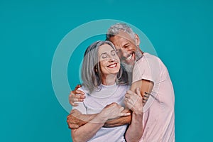 Loving senior couple bonding and smiling while standing together against blue background