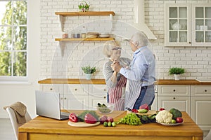 Loving senior couple having fun and dancing waltz while cooking healthy meal together