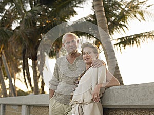 Loving Senior Couple Leaning Against Wall On Beach