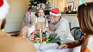 Loving senior grandparents give Christmas gift to happy girl granddaughter during festive dinner