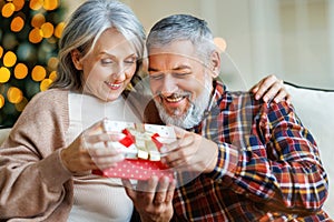 Loving senior man husband giving Christmas present gift box to happy surprised wife
