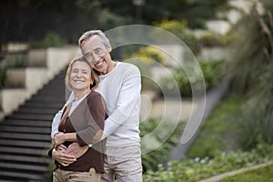 Loving Senior Man And Woman Hugging Standing In Park Outdoors