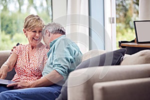 Loving Senior Retired Couple Sitting On Sofa At Home Enjoying Looking Through Family Photo Album