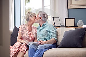 Loving Senior Retired Couple Sitting On Sofa At Home Enjoying Looking Through Family Photo Album