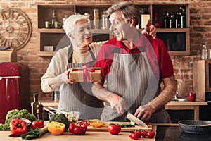 Loving senior woman congratulating husband with birthday, giving present in kitchen