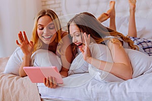 Loving sisters chilling in bed and having video chat with parents