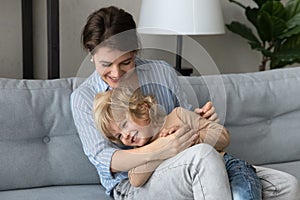 Loving smiling beautiful young mother tickling adorable laughing kid son.