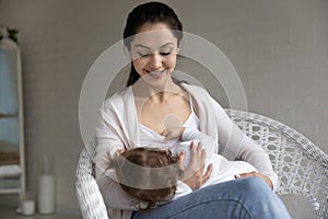 Loving smiling mother breastfeeding baby little daughter, sitting in chair