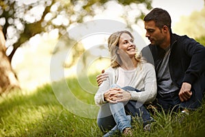 Loving their quiet moment together. a loving young couple sitting on the grass in a park.