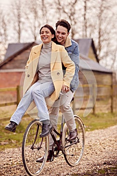 Loving Transgender Couple With Woman Riding On Handlebars Of Bike In Autumn Or Winter Countryside