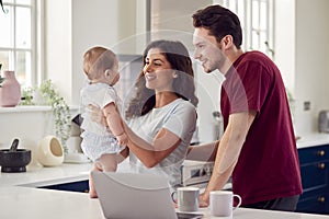 Loving Transgender Family With Baby At Home Together Looking At Laptop On Kitchen Counter