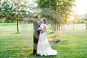Loving wedding couple hugging in a green summer dawn harden, looking utopically at each other
